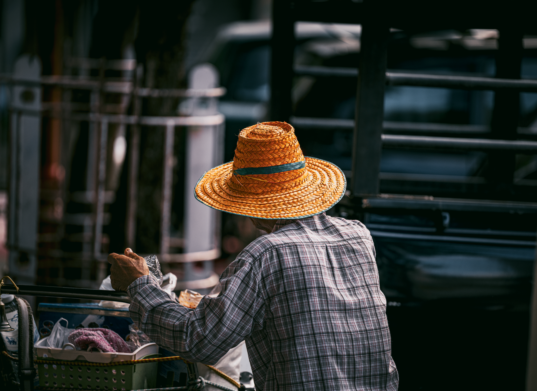 A street vendor in a straw hat pushing a cart along a Bangkok street, seen from behind